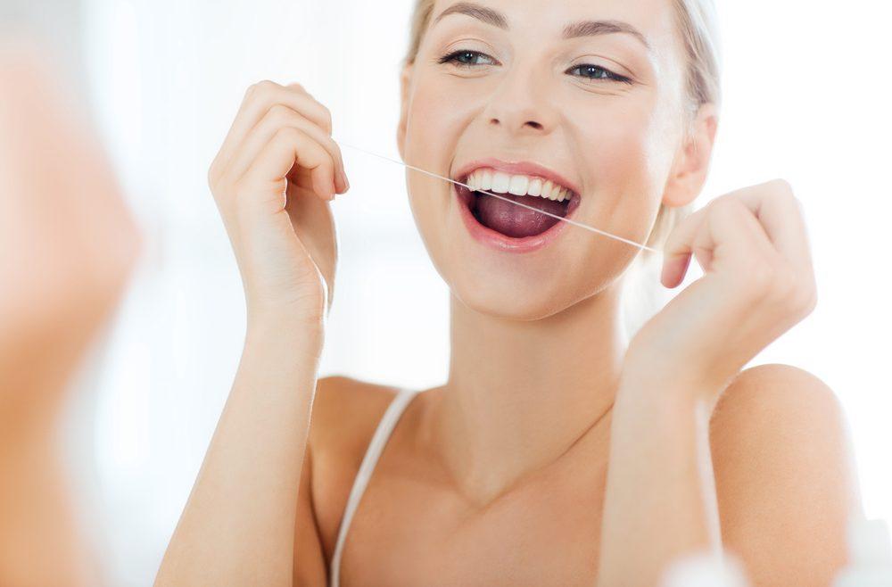 Young woman flossing her teeth in mirror